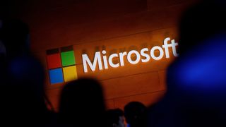 Microsoft logo and branding pictured on a wall with silhouettes in foreground.