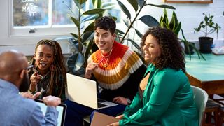 Female office workers in discussion with a male colleague in an open plan office space.