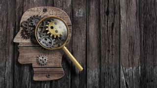 Wooden head silhouette mounted on planks with cogs inside it. A magnifying glass shows details of the cogs.