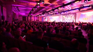 The crowd at Pure Storage's annual conference Pure Accelerate 2024, watching the opening keynote in Las Vegas. Decorative: The crowd is lit in orange and pink lighting.