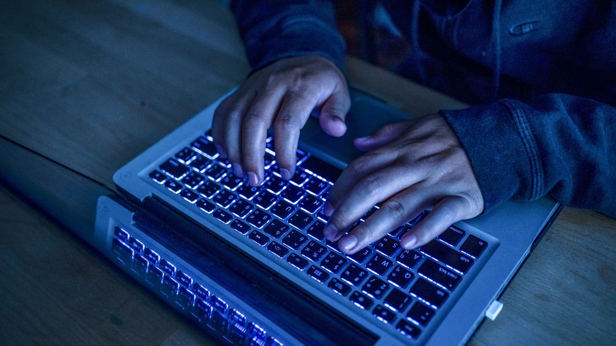 A cyber criminal using a laptop, with a close-up of their hands on the keyboard