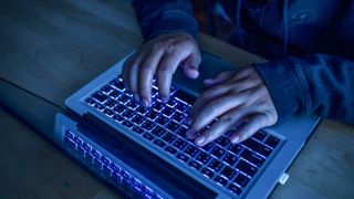 A cyber criminal using a laptop, with a close-up of their hands on the keyboard