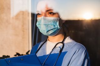 A forlorn doctor in a facemask, looking out the window