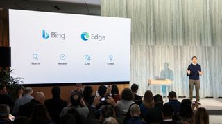 Yusuf Mehdi, Microsoft Corporate VP of modern life, search, and devices, speaking on stage next to a large screen displaying the Bing and Edge logos