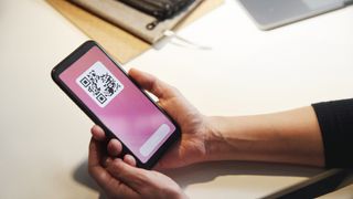 A person holding a smartphone with a QR code displayed on screen