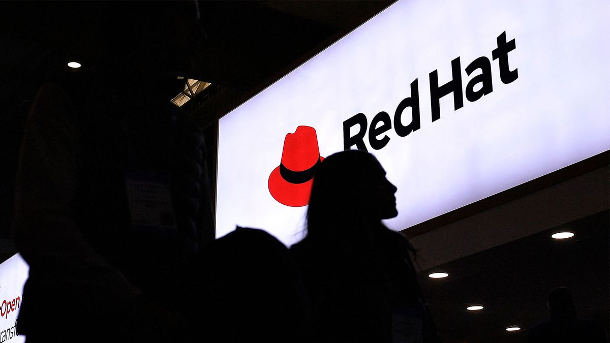 Mobile World Congress (MWC) attendee walks past Red Hat logo and branding pictured on a sign at the company&#039;s stall.