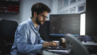 man sat working on computers with code displaying