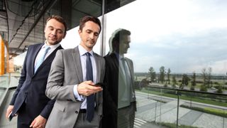A businessman looking over the shoulder of a colleague in order to secretly look at his phone screen