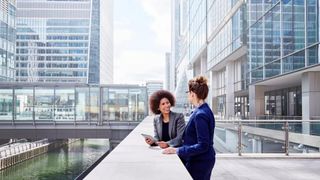 Two female colleagues chatting outside in front of large glass buildings